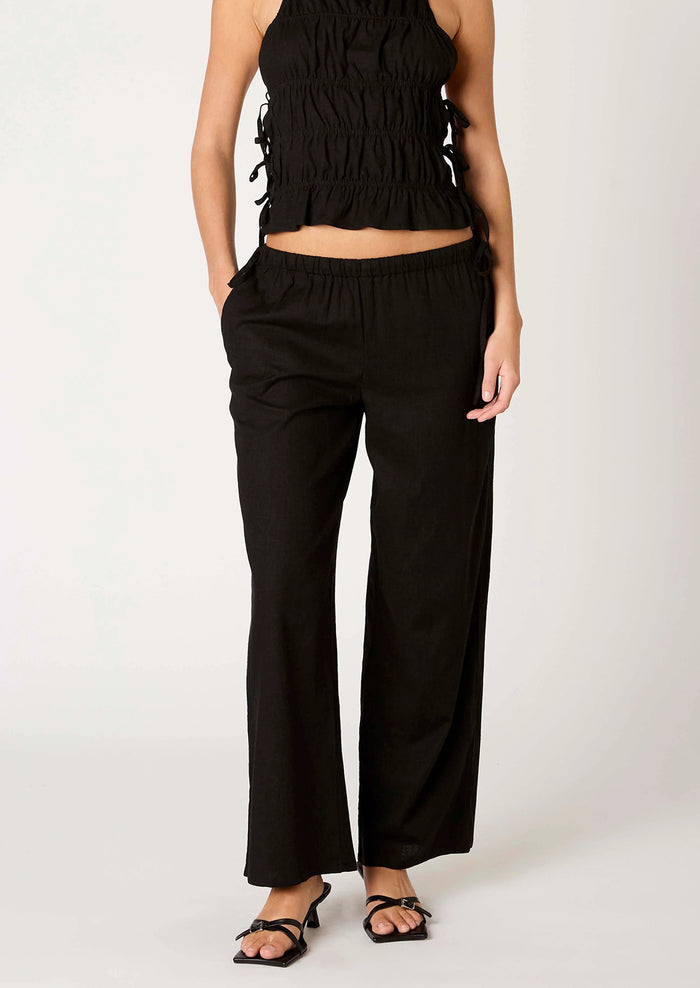 A person wearing a pair of relaxed black wide leg trousers with side tie detail at waist.
