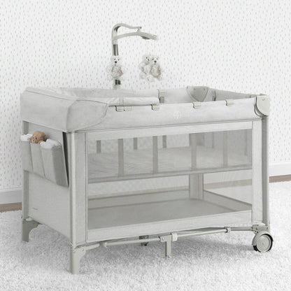 A babyGap Deluxe Play Yard with a infant inside, featuring mesh sides, a white frame, and wheels for mobility.