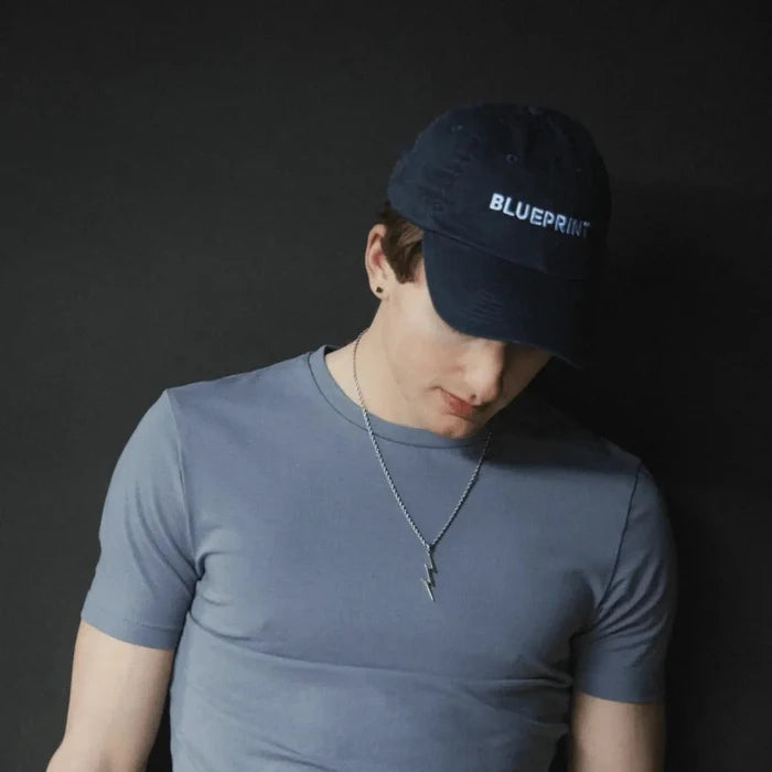 Person wearing Blueprint branded cap and blue shirt on dark background