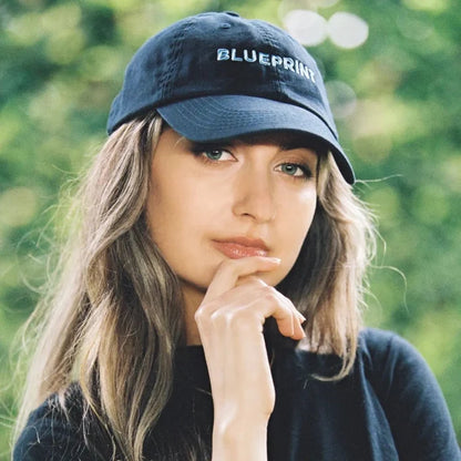 Woman wearing Blueprint branded cap outdoors with green background