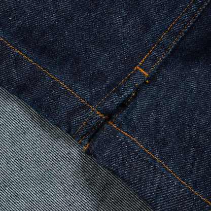 Close-up of dark indigo denim fabric with orange contrast stitching and a lighter gray denim section folded over.