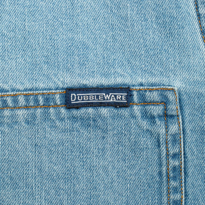 Close-up of a light blue denim garment showing a front pocket with contrast stitching and a small dark brand label reading Dubbleware.