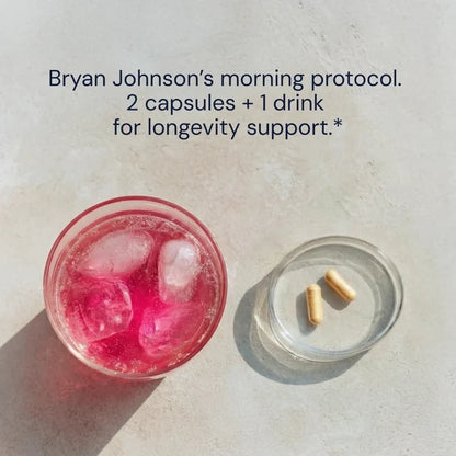 Glass of pink drink with ice and two capsules on a light surface, with text about Bryan Johnson's morning protocol.