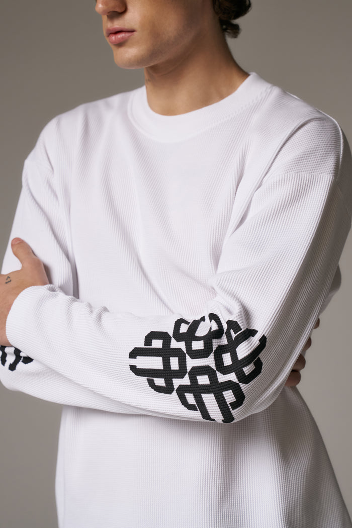 Person wearing a white long-sleeve shirt with black geometric patterns on the sleeves against a neutral background