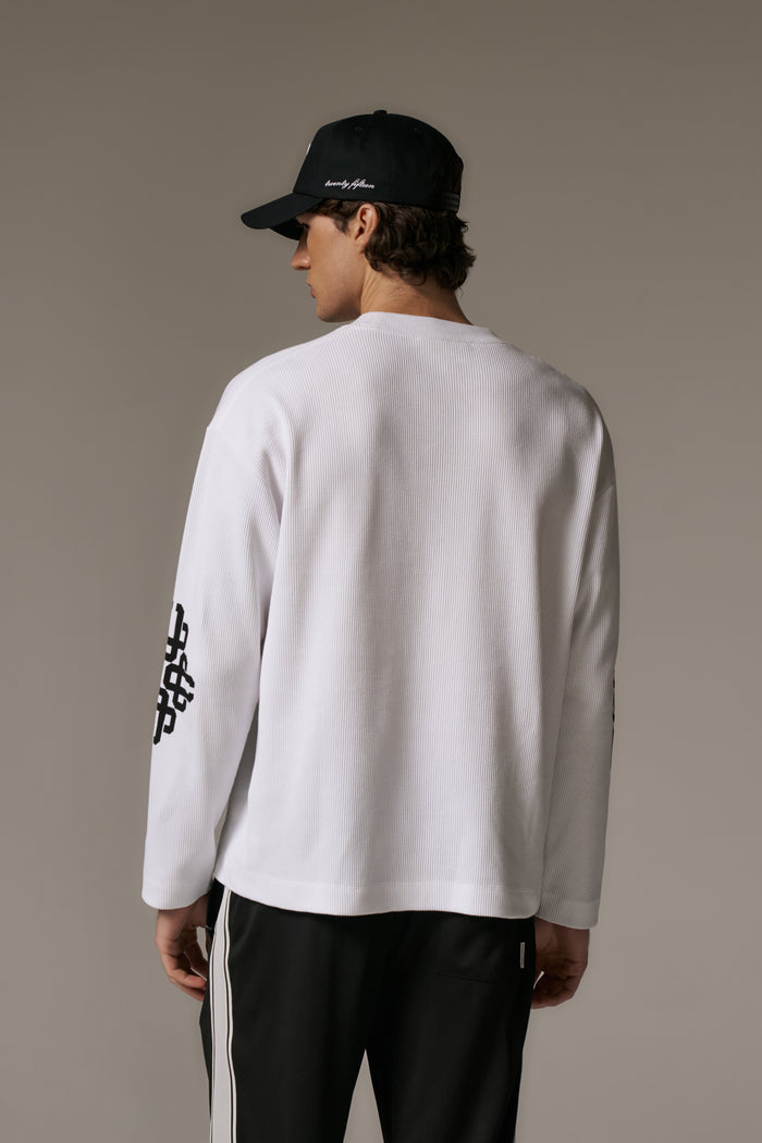 Person wearing a white long-sleeve t-shirt and black cap on a beige background