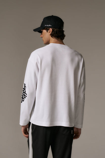 Person wearing a white long-sleeve t-shirt and black cap on a beige background