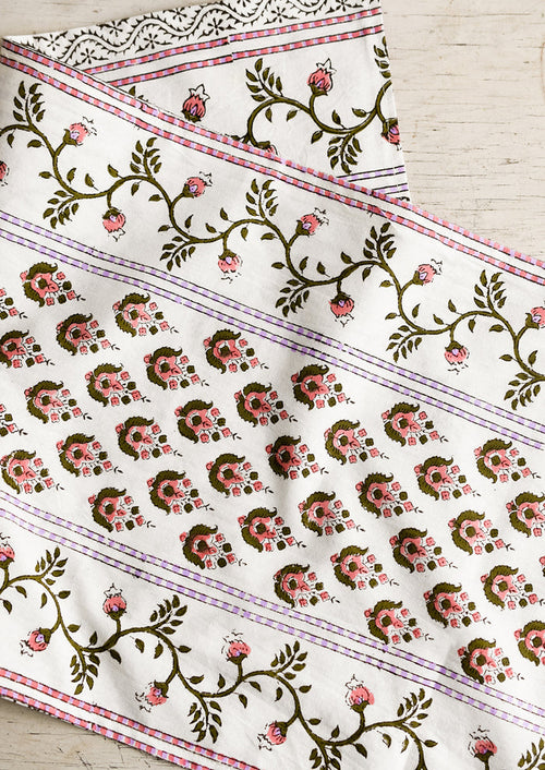 A block printed white table runner with pink, green and lavender floral print.