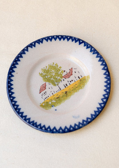 A plate with hand painted house motif and blue patterned rim.