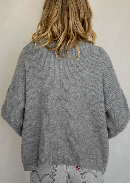 A woman wearing a heather grey cardigan sweater.