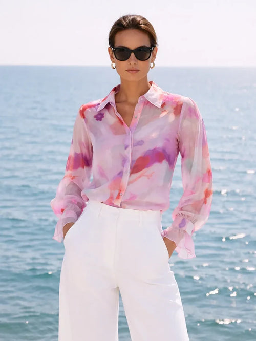 Woman wearing a colorful blouse and sunglasses by the ocean