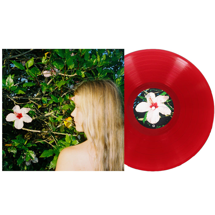 A red Oblivion vinyl record from Alice Phoebe Lou, featuring a hibiscus flower label, is displayed next to an album cover depicting Alice Phoebe Lou with her long blonde hair cascading as she stands before leafy green bushes adorned with white hibiscus flowers. Includes a download code for digital access.