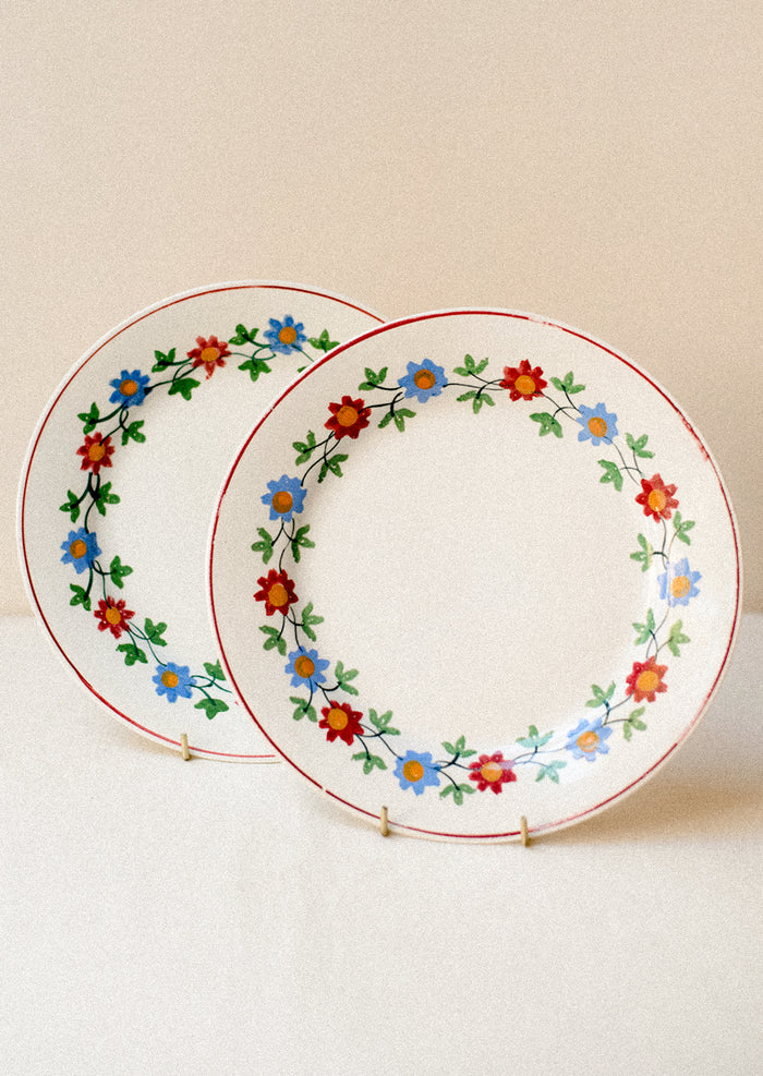 A pair of white plats with blue and red floral pattern around rim.