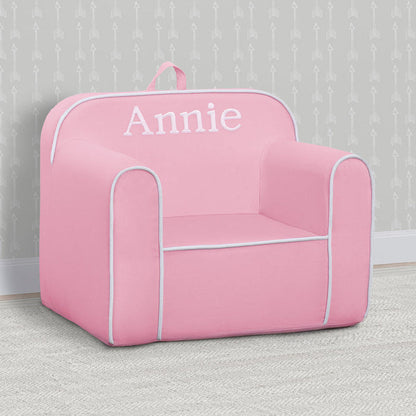Pink children's chair with 'Annie' printed on it against a gray wall.