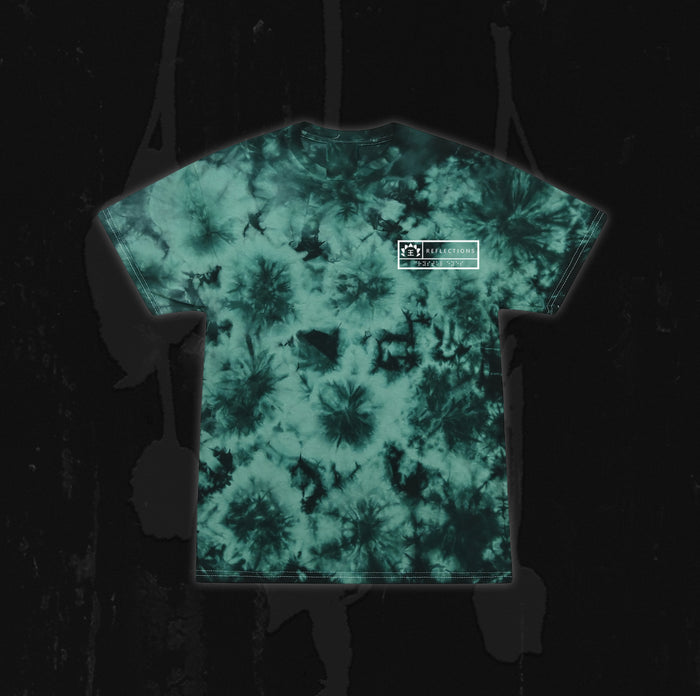 A green and black tie-dye t-shirt from Reflections, featuring a small white rectangular Crystal Eyes logo on the upper left chest, displayed on a dark, textured background.