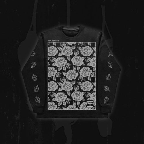 A black Reflections sweatshirt showcases a large white rose pattern on the front with “REFLECTIONS” text across the top, inspired by the ethereal style of Crystal Eyes. White leaf designs adorn both sleeves against a dark background.