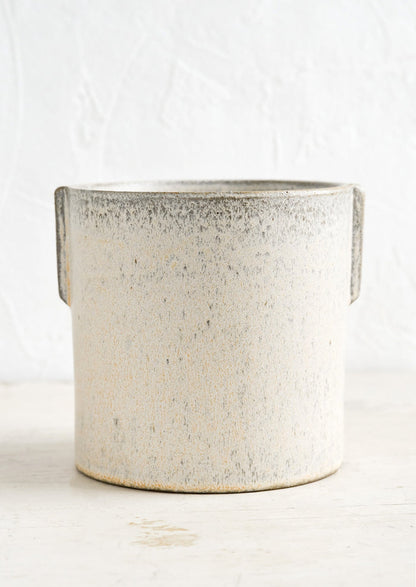 A neutral, speckled ceramic round planter with raised detailing at sides.